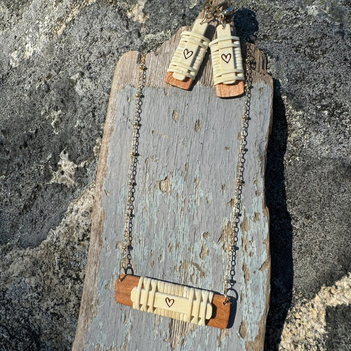 Handcrafted Slivers heart earrings paired with a horizontal necklace, both featuring woven holly wood and cherry wood bases, displayed on a piece of driftwood.