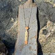 Handcrafted vertical Slivers heart necklace with woven holly wood and cherry wood base, draped on a piece of driftwood.