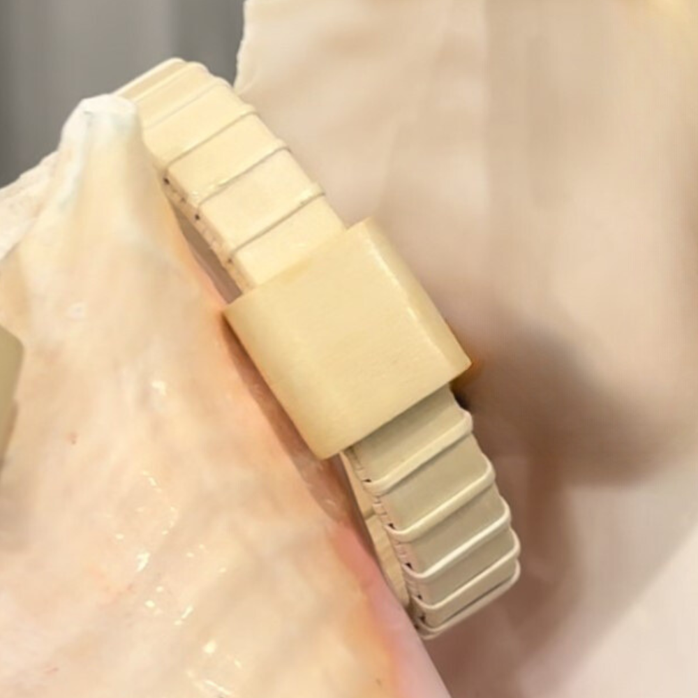 Handcrafted all-holly Island Cuff Bracelet with holly slider bead resting against a large seashell, showing the natural pale wood tones