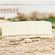 Handcrafted all-holly Legacy Cuff Bracelet resting on driftwood with a soft coastal marsh background, showing the pale natural wood tones of the wide woven band.