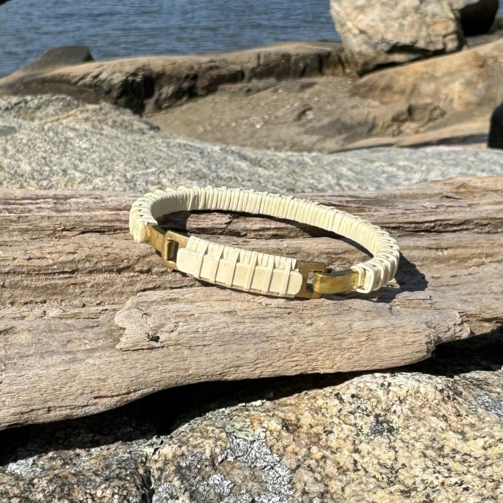 Handcrafted all-holly Nauti Clasp Bracelet with brass clasp resting on driftwood and coastal rocks in sunlight, showing the pale natural holly wood tones.
