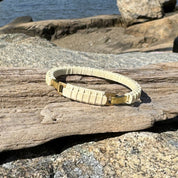Handcrafted all-holly Nauti Clasp Bracelet with brass clasp resting on driftwood and coastal rocks in sunlight, showing the pale natural holly wood tones.