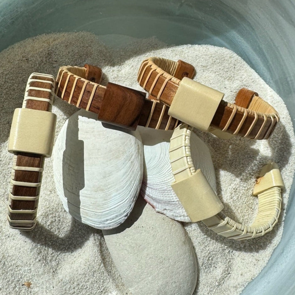 Handcrafted Vista cuff bracelets in rosewood and holly with holly wood slider beads, resting in sand with seashells.