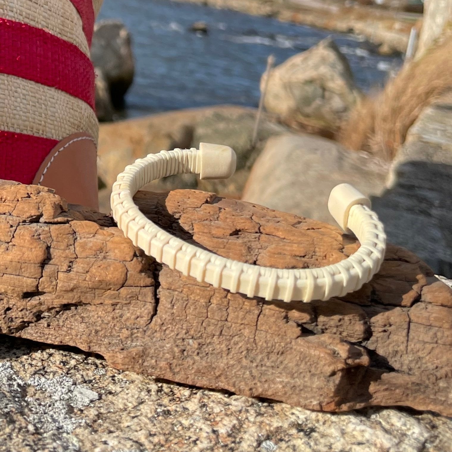 Handcrafted holly wood cuff bracelet with etched holly end caps, displayed on driftwood with rocks and water in the background.
