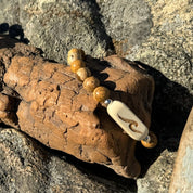 Close-up of a handcrafted Slivers wave bracelet with an etched holly wood bead and picture jasper stone beads, resting on driftwood.