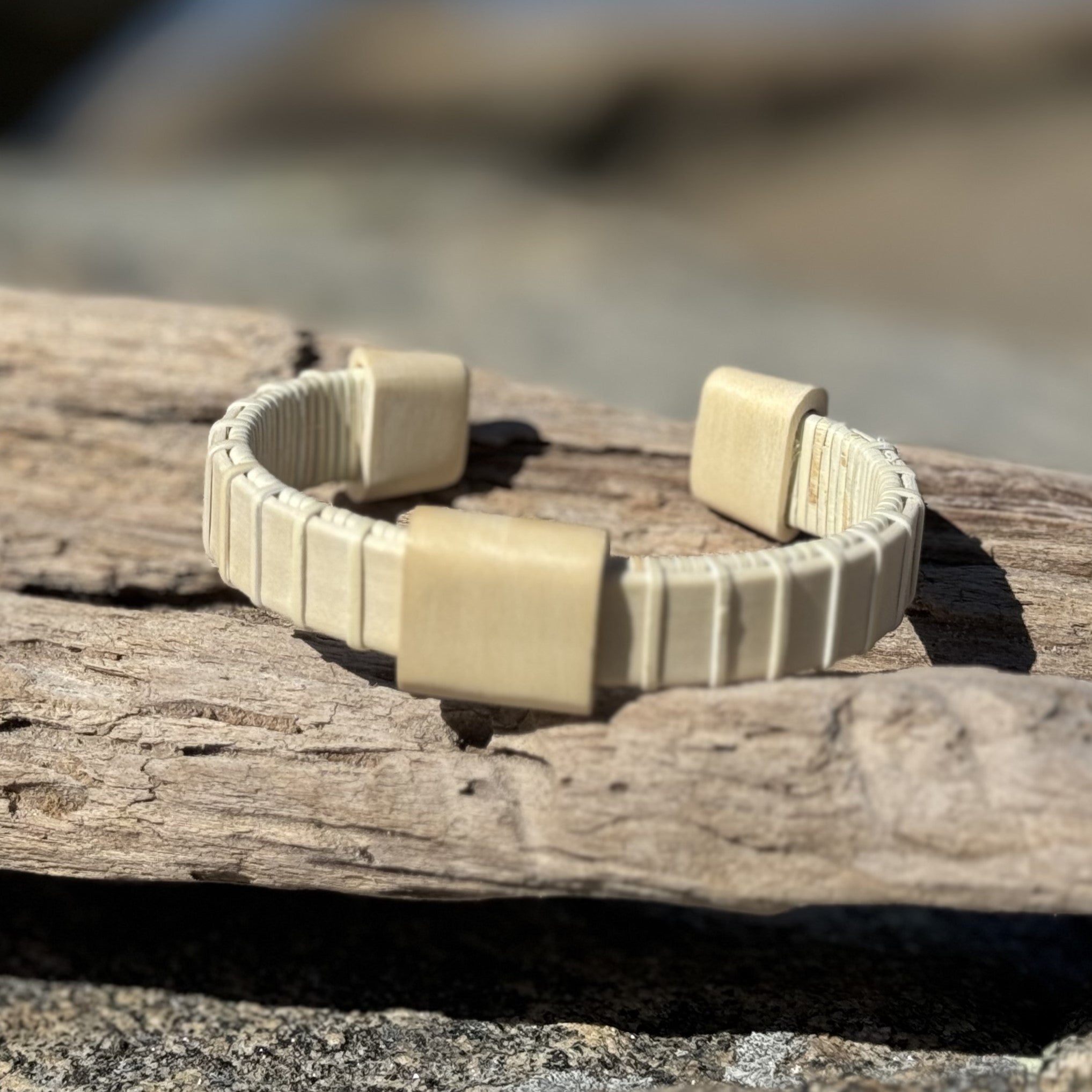 Handcrafted holly wood Vista cuff bracelet with a holly wood slider bead, resting on driftwood.