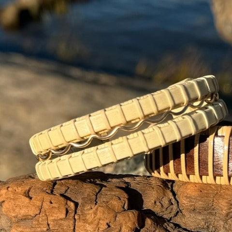 Two handcrafted holly wood Waves triple cuff bracelets with gold fill accent bands, stacked on rocks near the water.