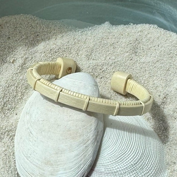 Handcrafted holly wood Bannister cuff bracelet with open-weave light weaver detailing, displayed on shells and sea stones — handmade by Military Spouse artisans in Stonington, Connecticut using American-made materials.