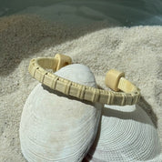 Handcrafted holly wood Clubhouse cuff bracelet with light weaver detailing, resting on a seashell in the sand — handmade by Military Spouse artisans in Stonington, Connecticut using American-made materials.