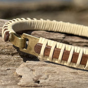 Close-up of the handcrafted mahogany Nauti Clasp Bracelet resting on driftwood, showing the brass clasp hardware and mahogany wood stave with holly weave detail.