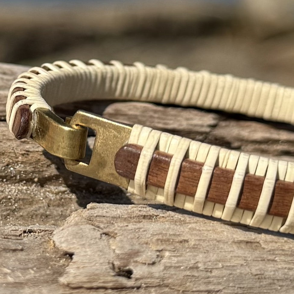Close-up of the handcrafted mahogany Nauti Clasp Bracelet resting on driftwood, showing the brass clasp hardware and mahogany wood stave with holly weave detail.