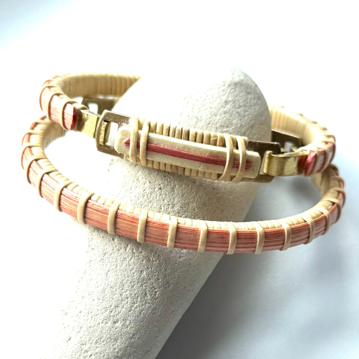 Bloom clasp bracelet in poppy red woven cane displayed on a white stone jewelry holder.