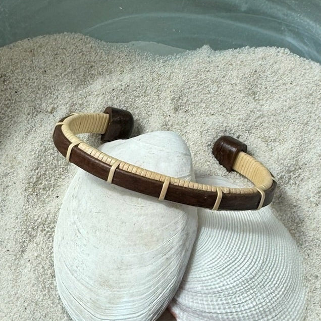 Handcrafted rosewood Bannister cuff bracelet with open-weave light weaver detailing, displayed on shells and sea stones — handmade by Military Spouse artisans in Stonington, Connecticut using American-made materials.