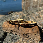 Two rosewood Breakers clasp bracelets resting on driftwood on granite rocks with water in the background.