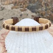 Single rosewood Clubhouse cuff bracelet resting on a white seashell outdoors.