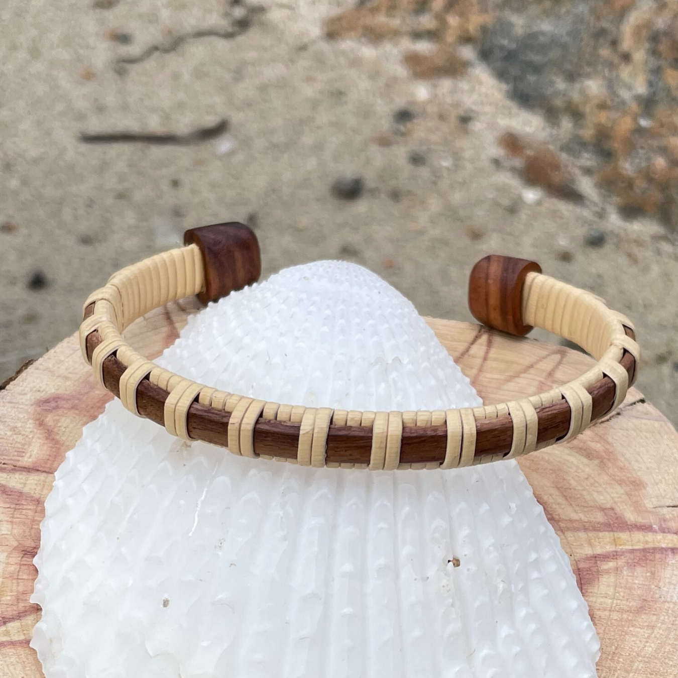 Single rosewood Clubhouse cuff bracelet resting on a white seashell outdoors.