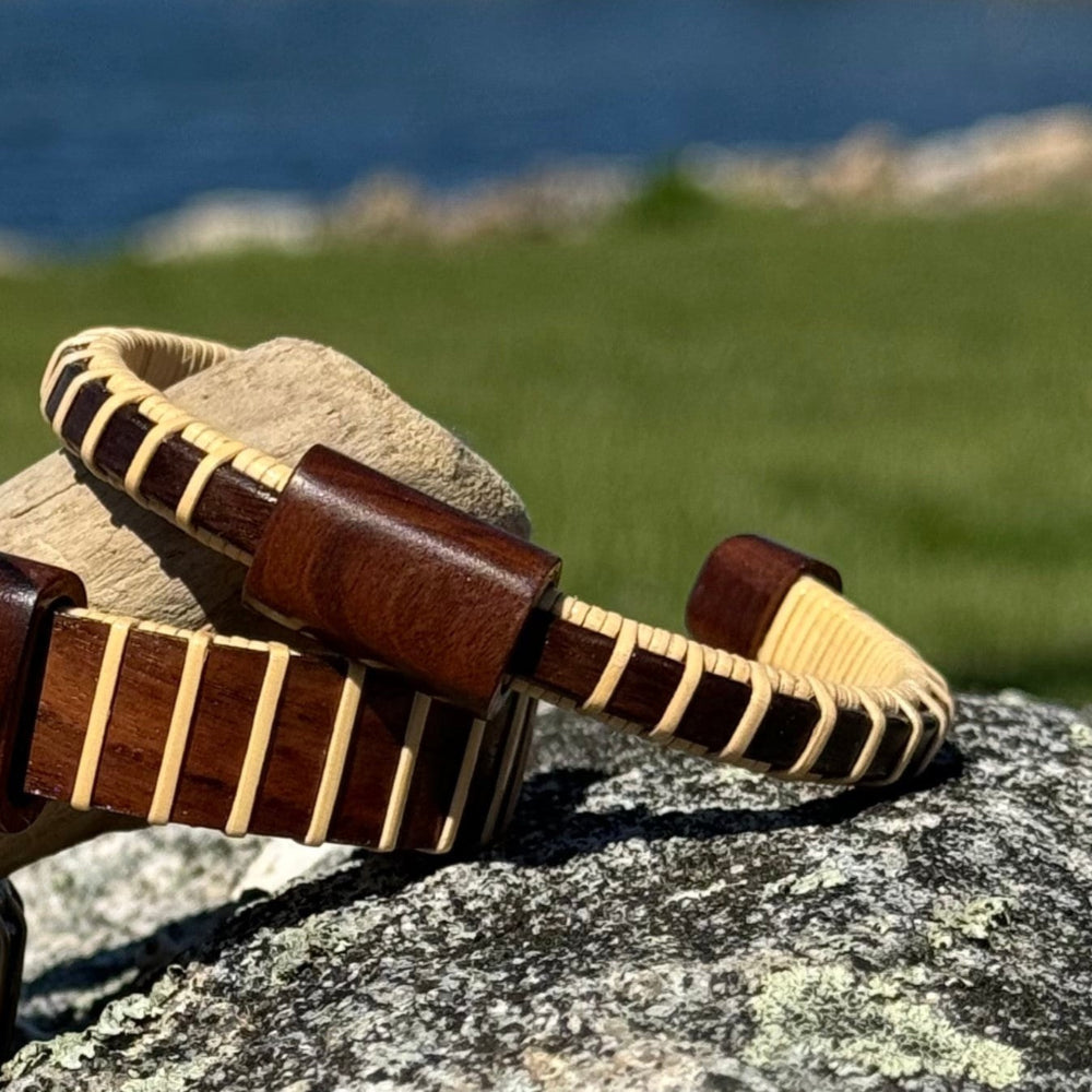 Single rosewood Cove cuff bracelet with rosewood slider resting on granite rocks with ocean and green hillside in the background.