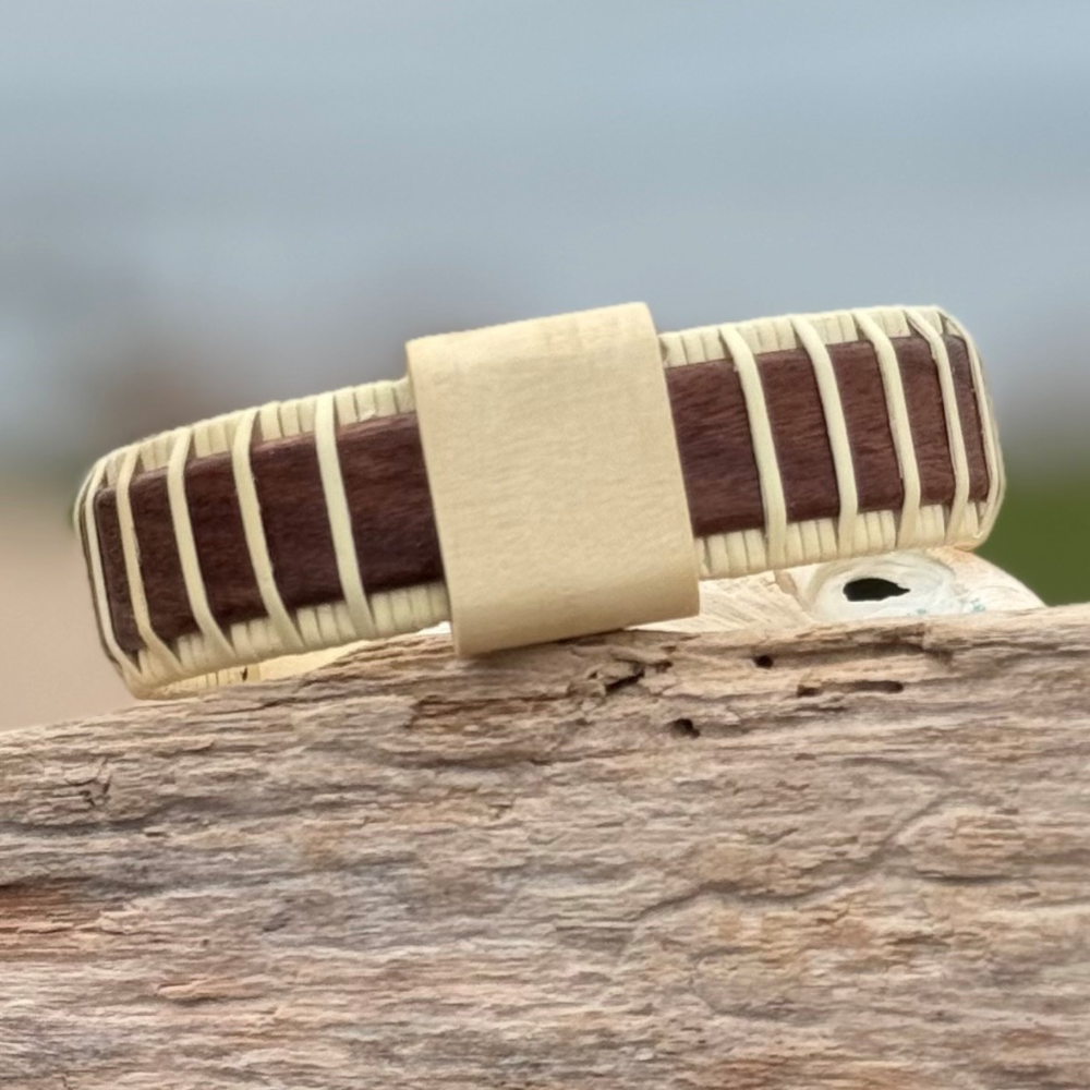 Handcrafted rosewood Island Cuff Bracelet with holly slider bead resting on driftwood outdoors.