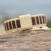 Handcrafted rosewood Island Cuff Bracelet with holly slider bead resting on driftwood outdoors.