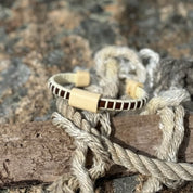 Single rosewood Cove cuff bracelet with holly slider resting on nautical rope on granite rocks.