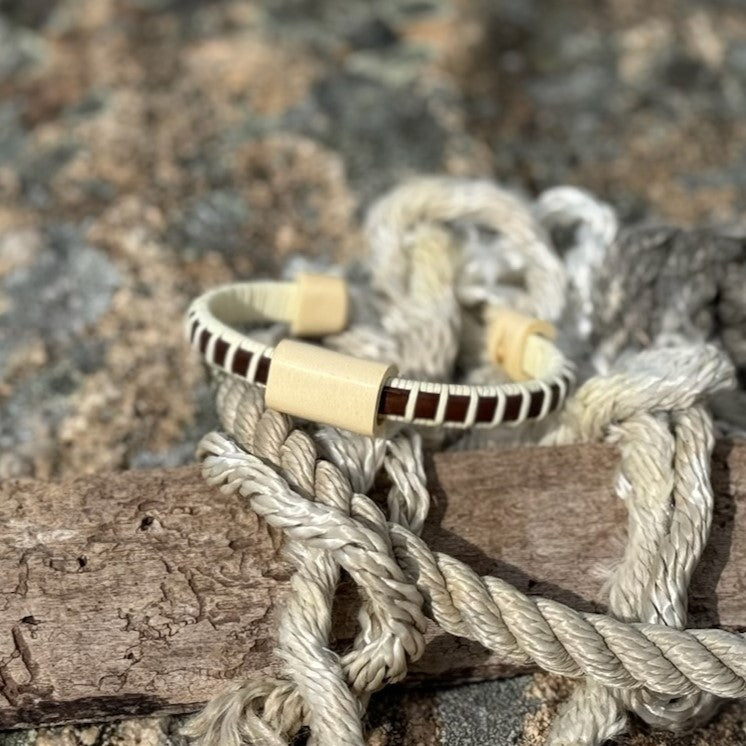 Single rosewood Cove cuff bracelet with holly slider resting on nautical rope on granite rocks.