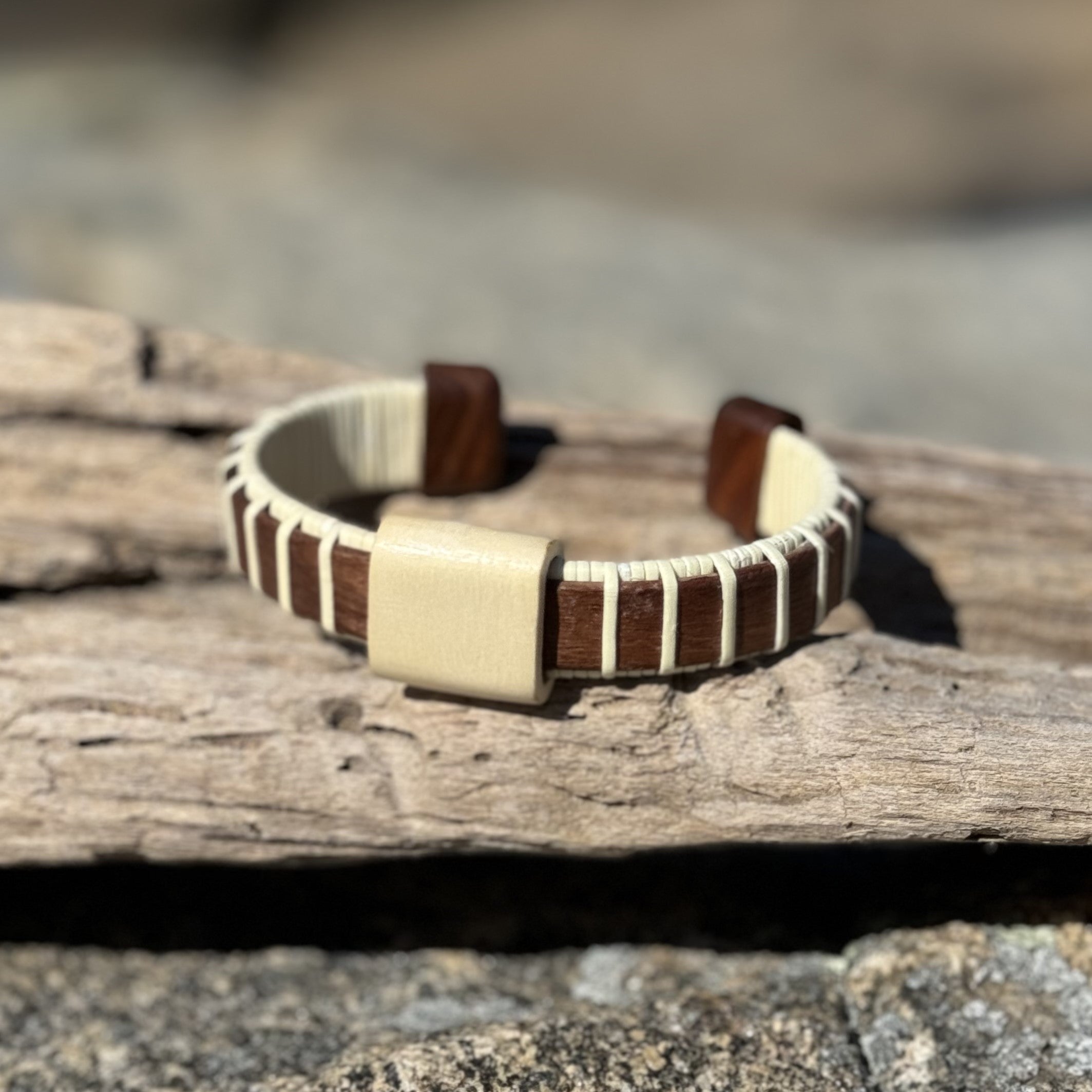 Handcrafted rosewood Vista cuff bracelet with a holly wood slider bead, resting on driftwood.