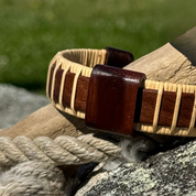 Handcrafted rosewood Island Cuff Bracelet with matching rosewood slider bead resting on coiled rope and rock with driftwood, highlighting the rich warm tones of the rosewood.