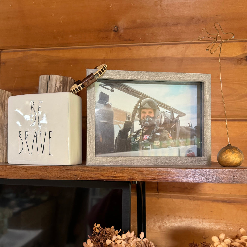Handcrafted rosewood Love In the Air Etched Cuff Bracelet displayed on a shelf alongside a framed pilot photo, a Be Brave ceramic, and a gold wire airplane sculpture — a meaningful gift for aviation families.