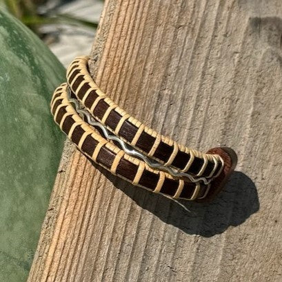 Handcrafted rosewood Waves triple cuff bracelet with a sterling silver accent band, resting on driftwood.