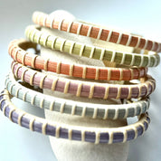 Six Bloom clasp bracelets in amaryllis, hydrangea, lilac, orchid, poppy, and tulip spring colors stacked on a jewelry display.