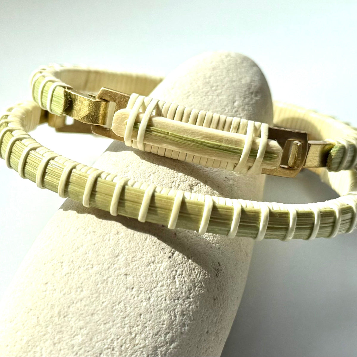 Bloom clasp bracelet in tulip green woven cane displayed on a white stone jewelry holder.