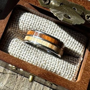 Handcrafted 8mm tungsten ring with cherry and rosewood double wood inlay resting on burlap lining inside an engraved wooden gift box.