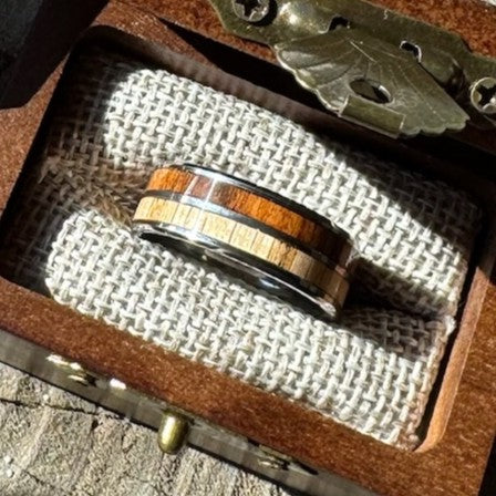 Handcrafted 8mm tungsten ring with cherry and rosewood double wood inlay resting on burlap lining inside an engraved wooden gift box.