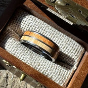 Handcrafted 8mm tungsten ring with cherry and white oak double wood inlay resting on burlap lining inside an engraved wooden gift box