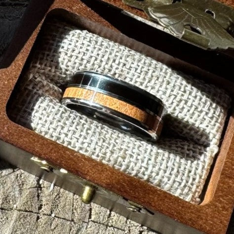 Handcrafted 8mm tungsten ring with ebony and cherry double wood inlay resting on burlap lining inside an engraved wooden gift boxr