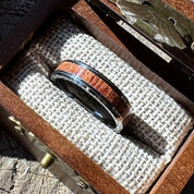 Handcrafted tungsten ring with mahogany wood inlay resting on burlap lining inside an open engraved wooden gift box