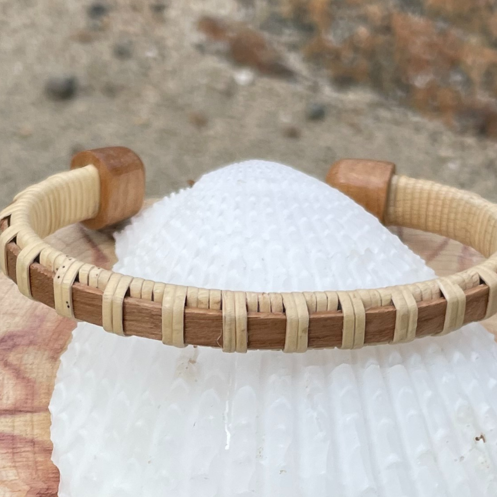 Single walnut Clubhouse cuff bracelet resting on a white seashell outdoors.