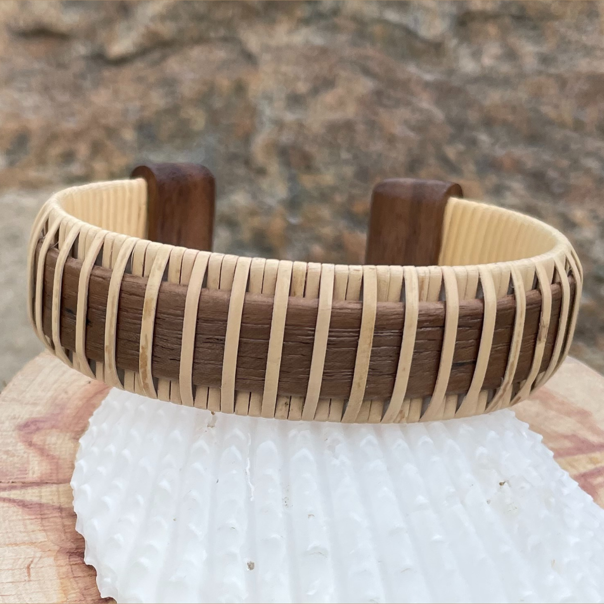 Handcrafted walnut Legacy Cuff Bracelet with walnut end caps resting on a white textured stone, showing the rich dark wood stave and wide handwoven band construction.