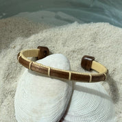Handcrafted walnut wood Bannister cuff bracelet with open-weave light weaver detailing, displayed on shells and sea stones — handmade by Military Spouse artisans in Stonington, Connecticut using American-made materials.