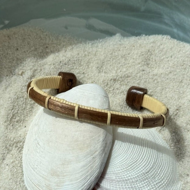 Handcrafted walnut wood Bannister cuff bracelet with open-weave light weaver detailing, displayed on shells and sea stones — handmade by Military Spouse artisans in Stonington, Connecticut using American-made materials.