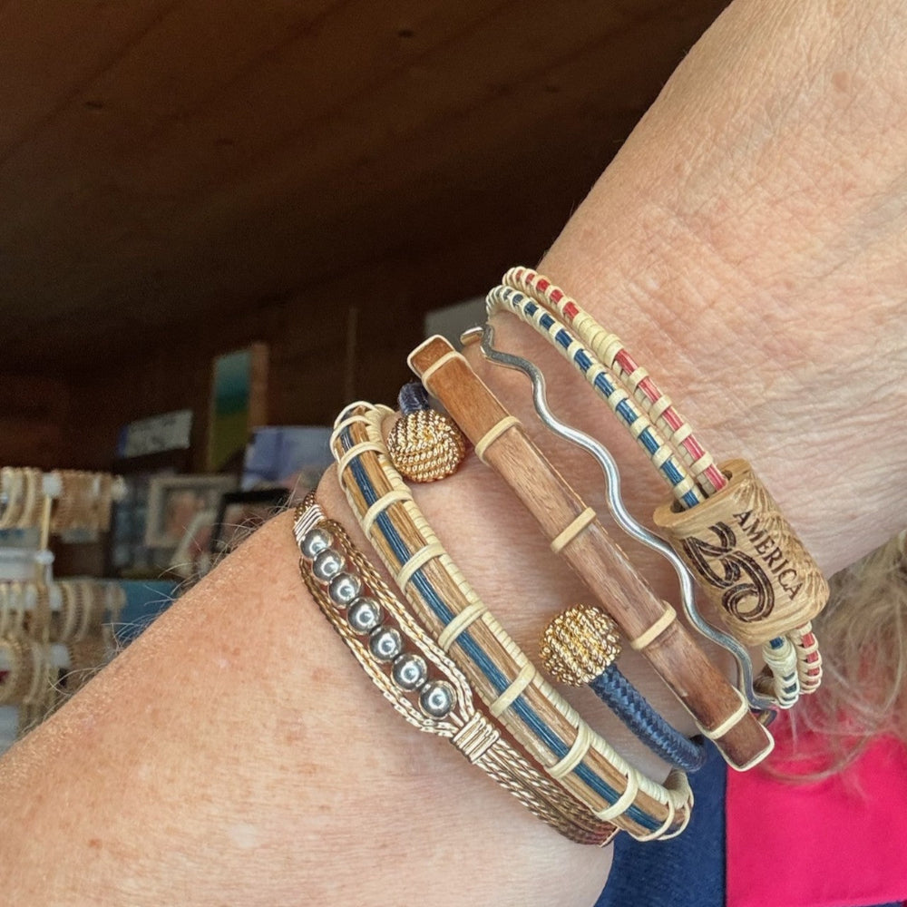 America 250 clasp bracelet worn in a stacked bracelet display on a wrist, shown alongside other wood and woven bracelets