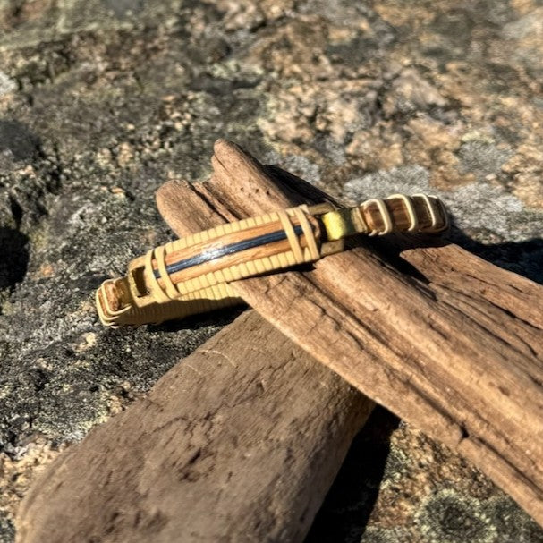 Close-up of the brass clasp detail on a white oak and blue bamboo bracelet resting on driftwood