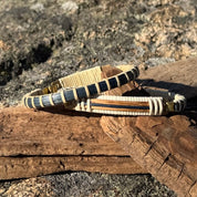 Two white oak and blue bamboo clasp bracelets resting on a piece of driftwood outdoors in sunlight