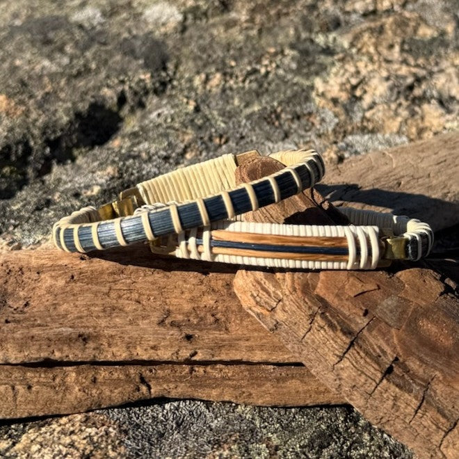 Two white oak and blue bamboo clasp bracelets resting on a piece of driftwood outdoors in sunlight