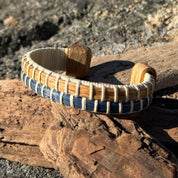 White oak and navy bamboo cuff bracelet resting on driftwood outdoors in sunlight.