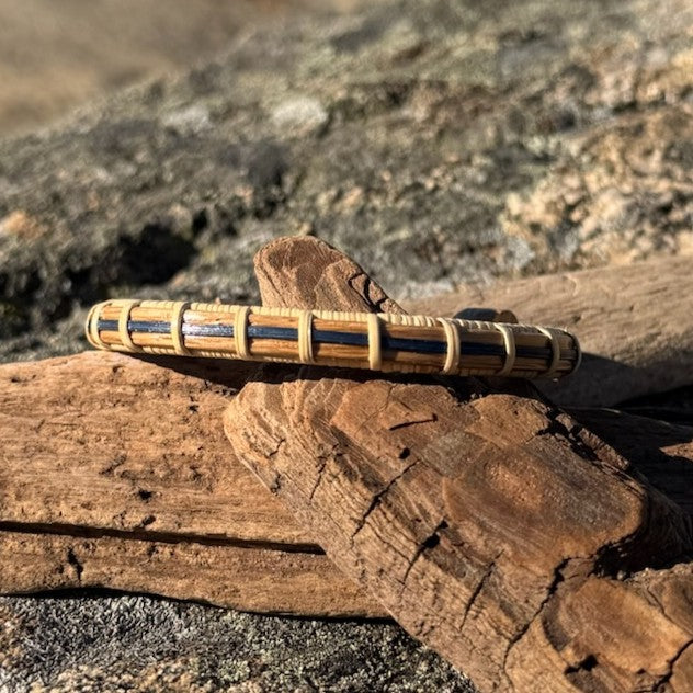 Side profile of the handcrafted white oak and navy bamboo Patriot Cuff Bracelet resting on driftwood, showing the open-stave weave construction, part of the America250 Collection by Stonington Designs.