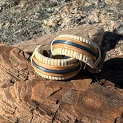 Handcrafted Patriot Small Hoop Earrings in white oak and hand-dyed navy bamboo resting on driftwood against coastal rocks, part of the America250 Collection made by military spouse artisans at Stonington Designs.