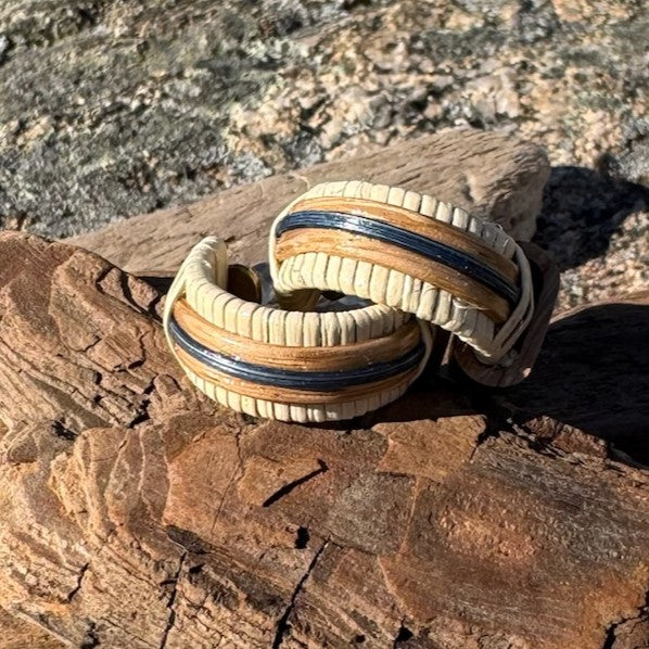 Handcrafted Patriot Small Hoop Earrings in white oak and hand-dyed navy bamboo resting on driftwood against coastal rocks, part of the America250 Collection made by military spouse artisans at Stonington Designs.