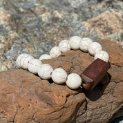 Beachcomber bracelet with white turquoise stones and a rectangular wood bead resting on driftwood and granite rocks.
