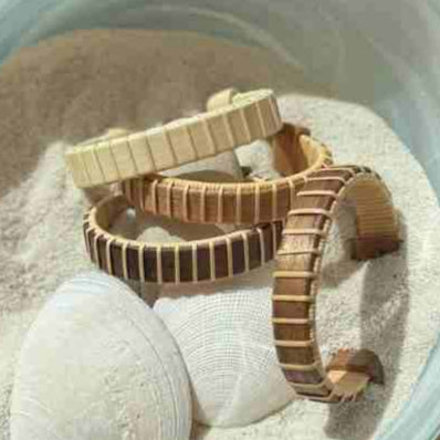 Handcrafted Maverick Cuff Bracelets in holly, cherry, and rosewood variants arranged on seashells and sand, made by military spouse artisans at Stonington Designs.